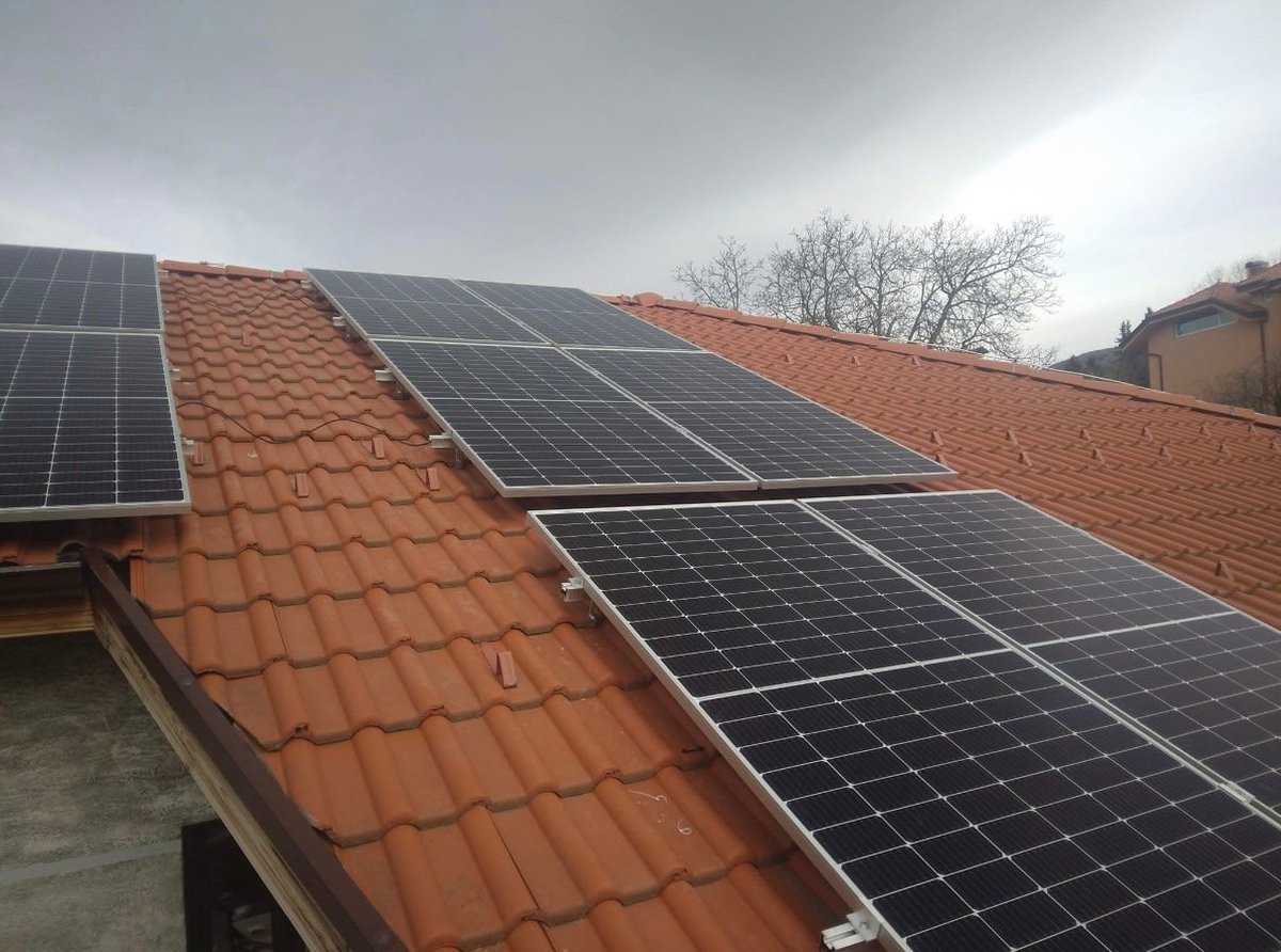 Solar panels installed on a brick building roof with clay tiles under cloudy sky
