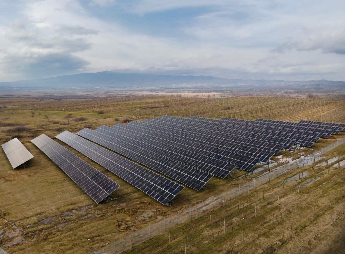 Large-scale solar panel array in remote landscape with mountains visible in the distance under cloudy sky