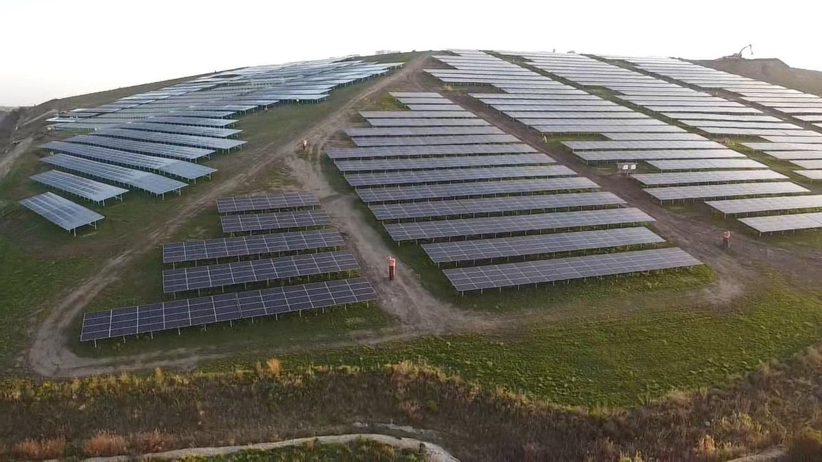 Aerial view of a large solar panel farm with rows of photovoltaic panels on rolling green hillside
